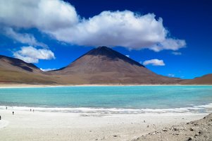 Ein Berg hinter einem türkisblauen See in Bolivien mit einer weißen Schäfchenwolke